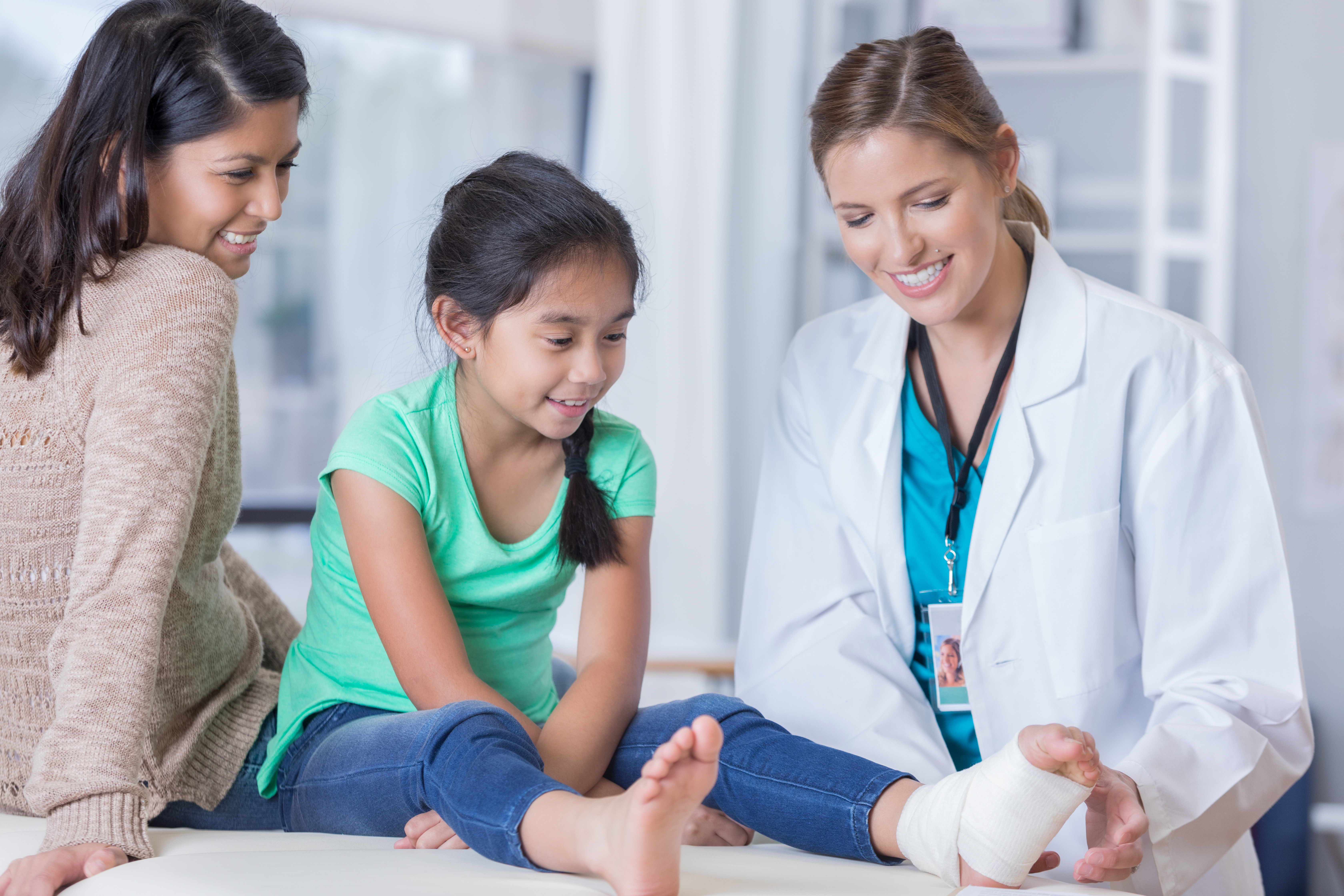 Pediatrician wraps a young girl's sprained ankle. The patient's mom is sitting next to the patient.